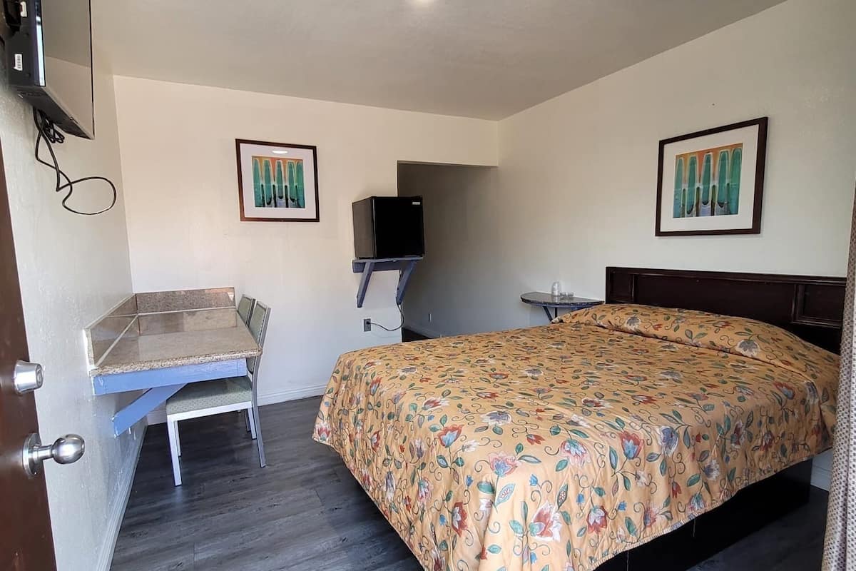 A bedroom with a bed, a desk, a chair, a television, and two framed pictures on the wall.