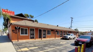 A motel with a simple facade, a parking lot, and a clear sky. - Carlo Motel (Los Angeles)
