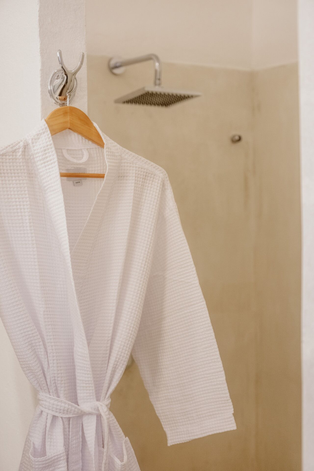 A white robe hanging on a wooden hanger in a bathroom with a shower.