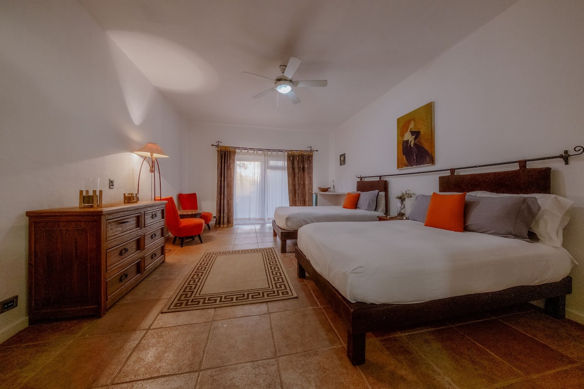 A bedroom with two beds, a wooden dresser, a desk, a chair, and a ceiling fan.
