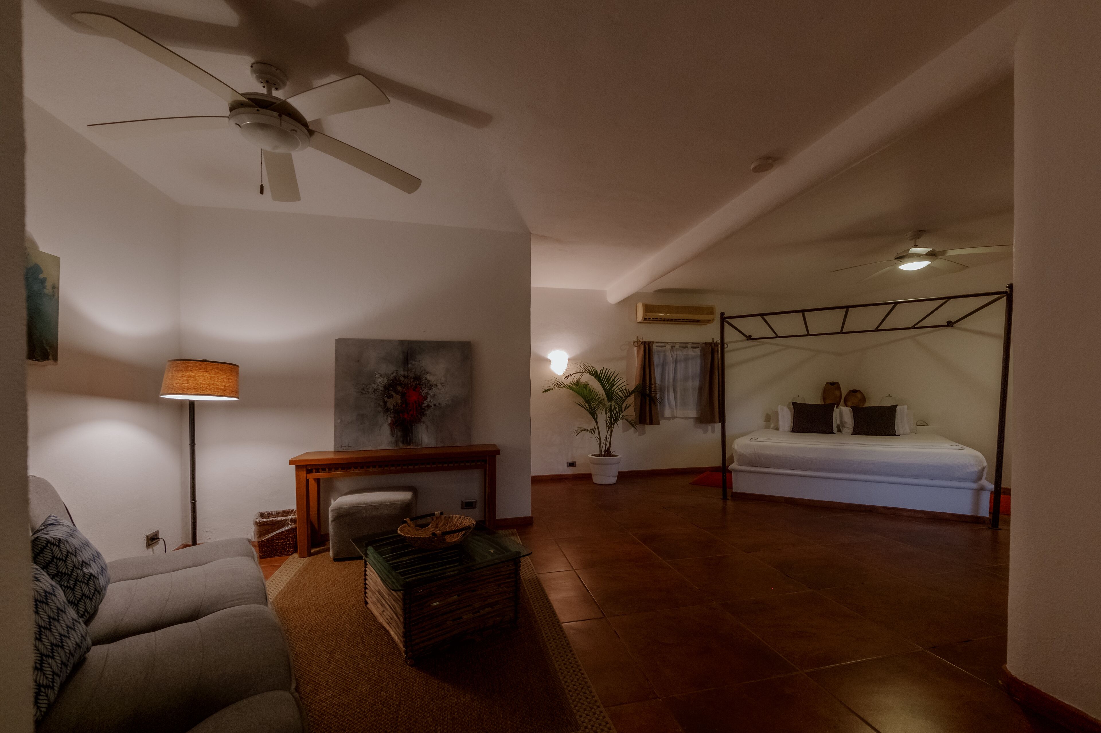 A spacious living area with a sofa, a coffee table, a ceiling fan, and a bed with a metal frame.