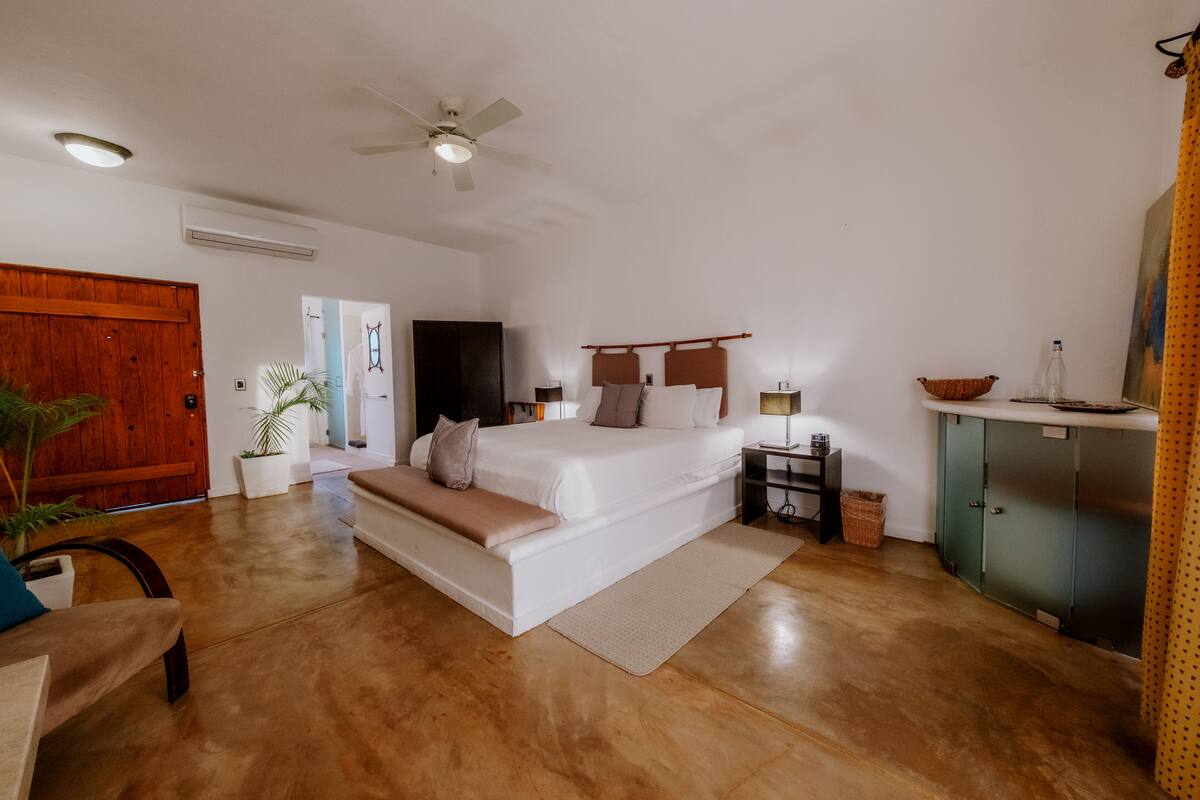 A bedroom with a large bed, a ceiling fan, a wooden door, and a green cabinet.