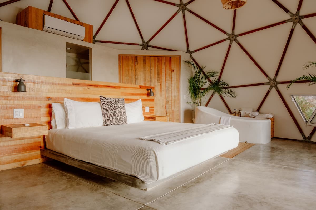 A modern bedroom with a wooden headboard, a large bed with white linens, a bedside table, and a built-in bench.