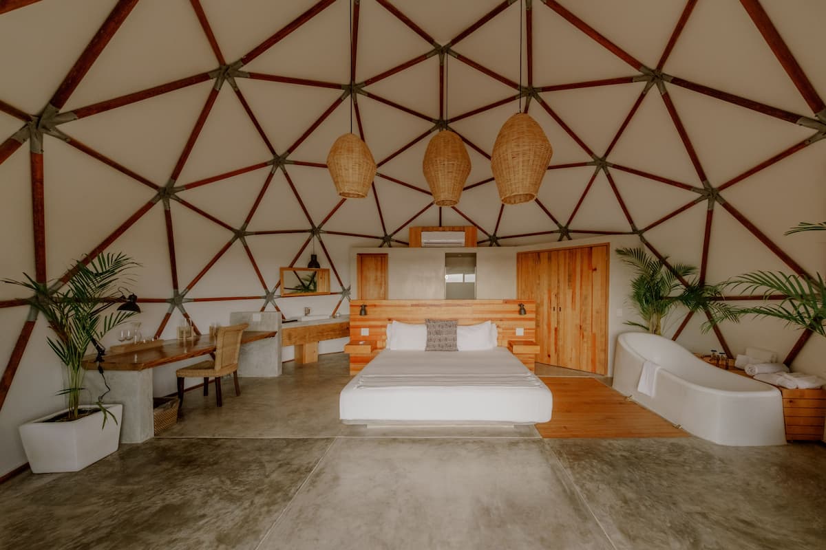 A modern bedroom with a geometric ceiling, a large bed, a wooden desk, and a bathtub.