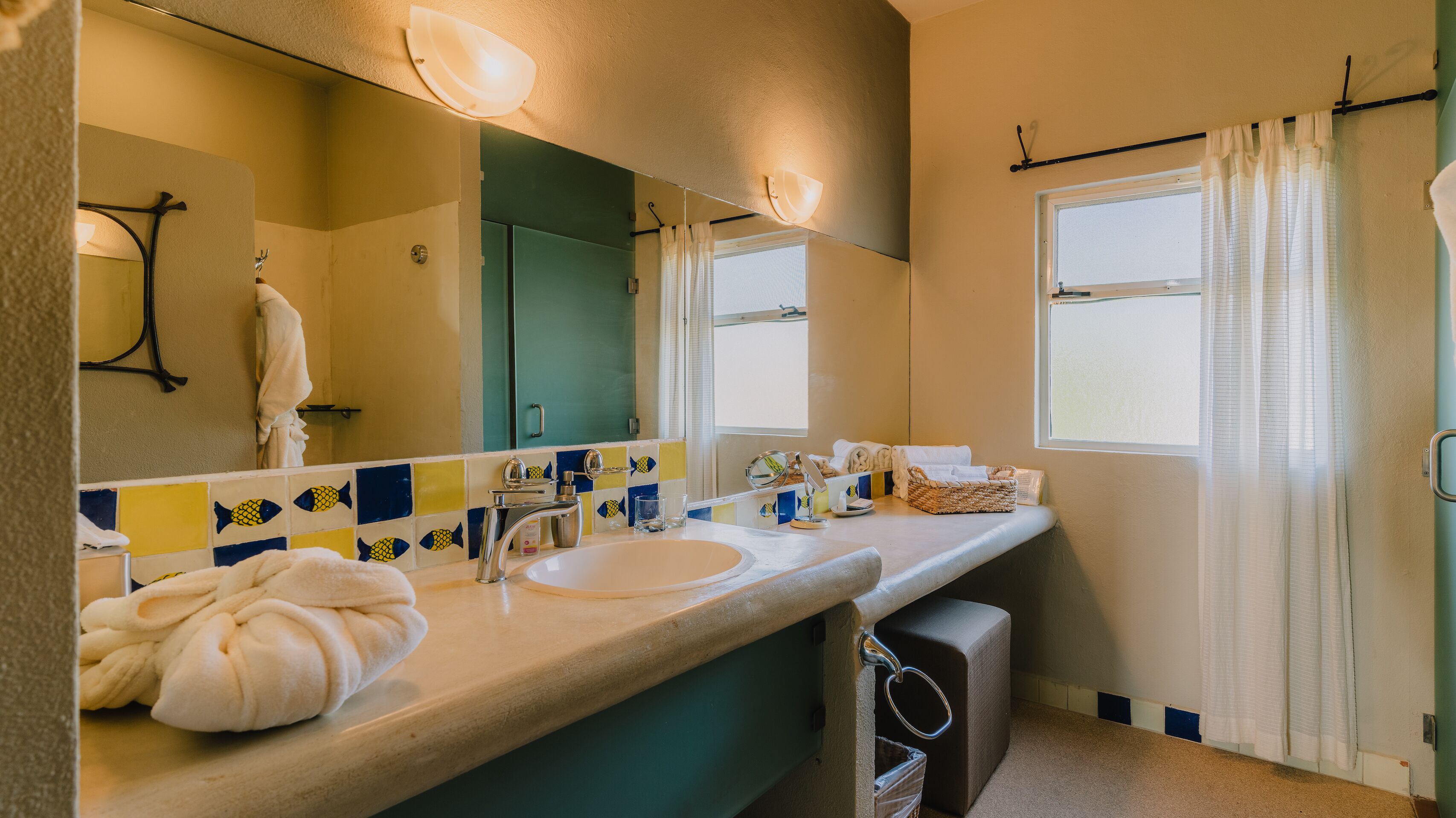Un baño con un espejo grande, un lavabo, un inodoro y una ventana con cortinas.