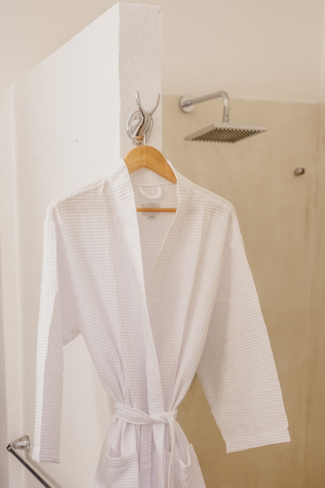 Un albornoz blanco colgado de una percha de madera en un baño con ducha.