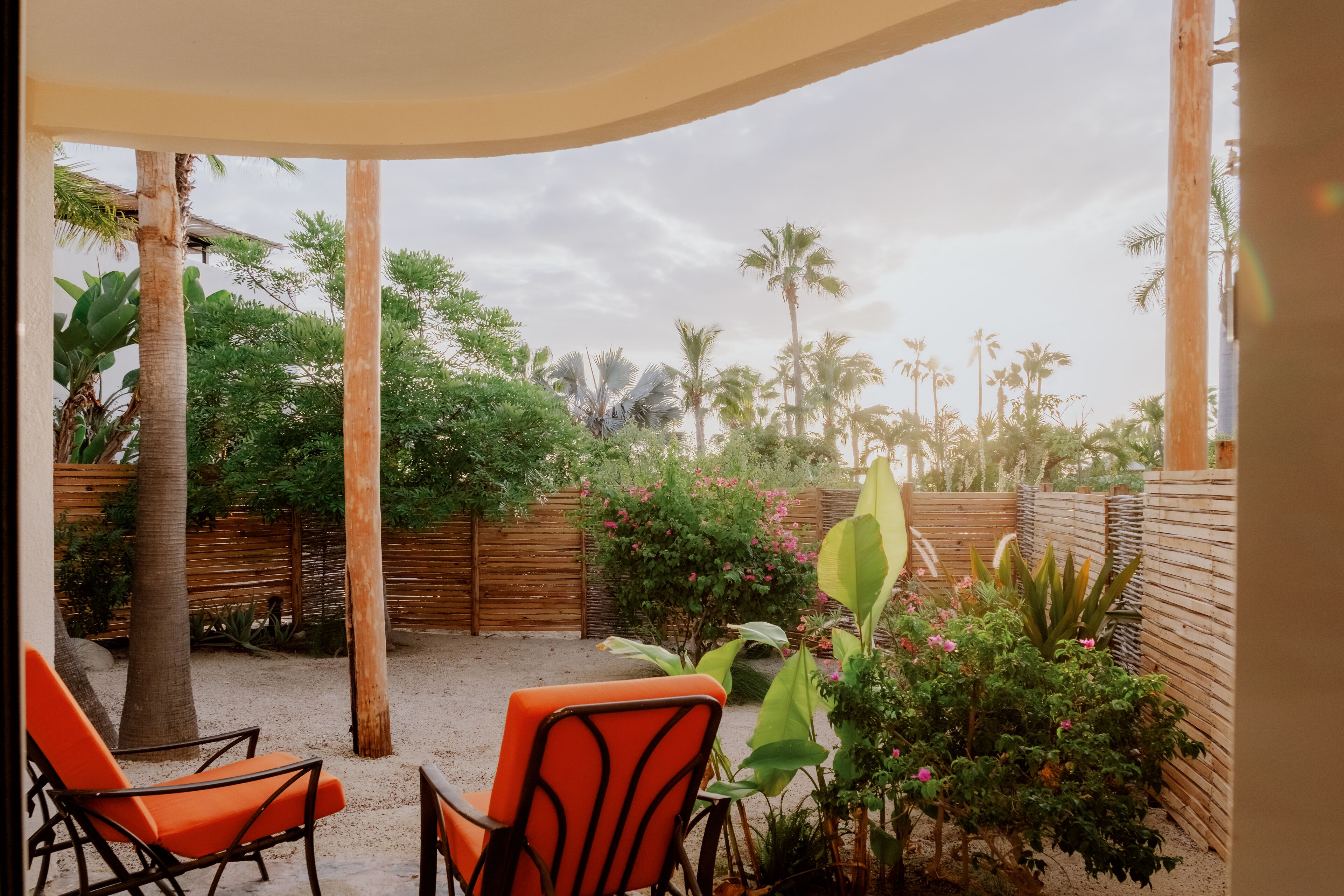 Un patio al aire libre con dos sillones naranjas, una valla de madera y diversas plantas.