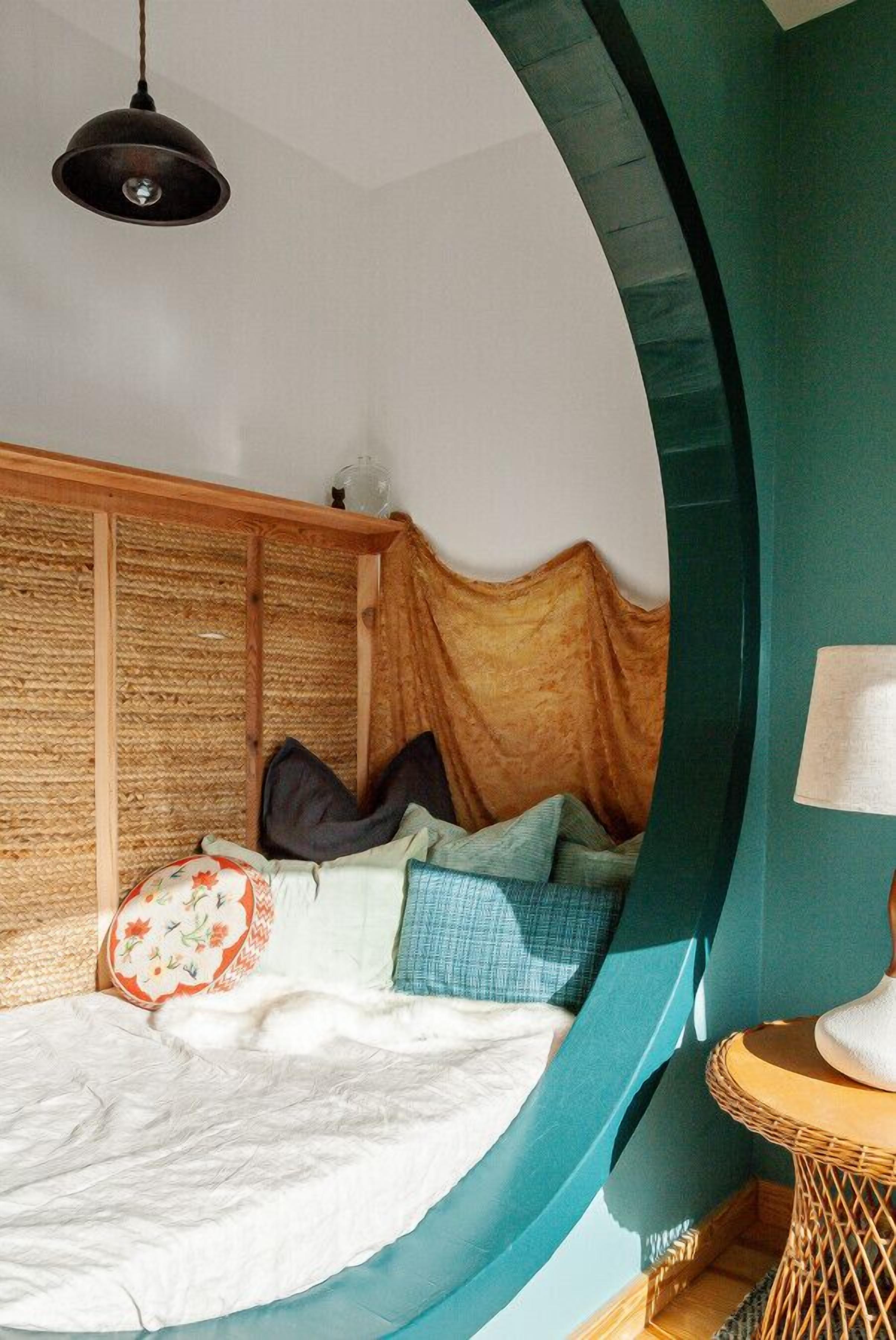A circular room with a bed, a hanging light fixture, and a small round table with a lamp.