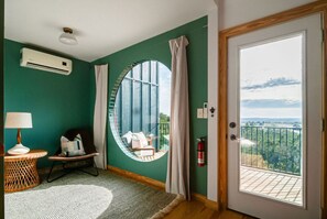 A room with a large circular window, a round table, a chair, and a view of a balcony with a railing. - Blue Sage No. 12 - The Long Loft Hideaway (Fredericksburg)