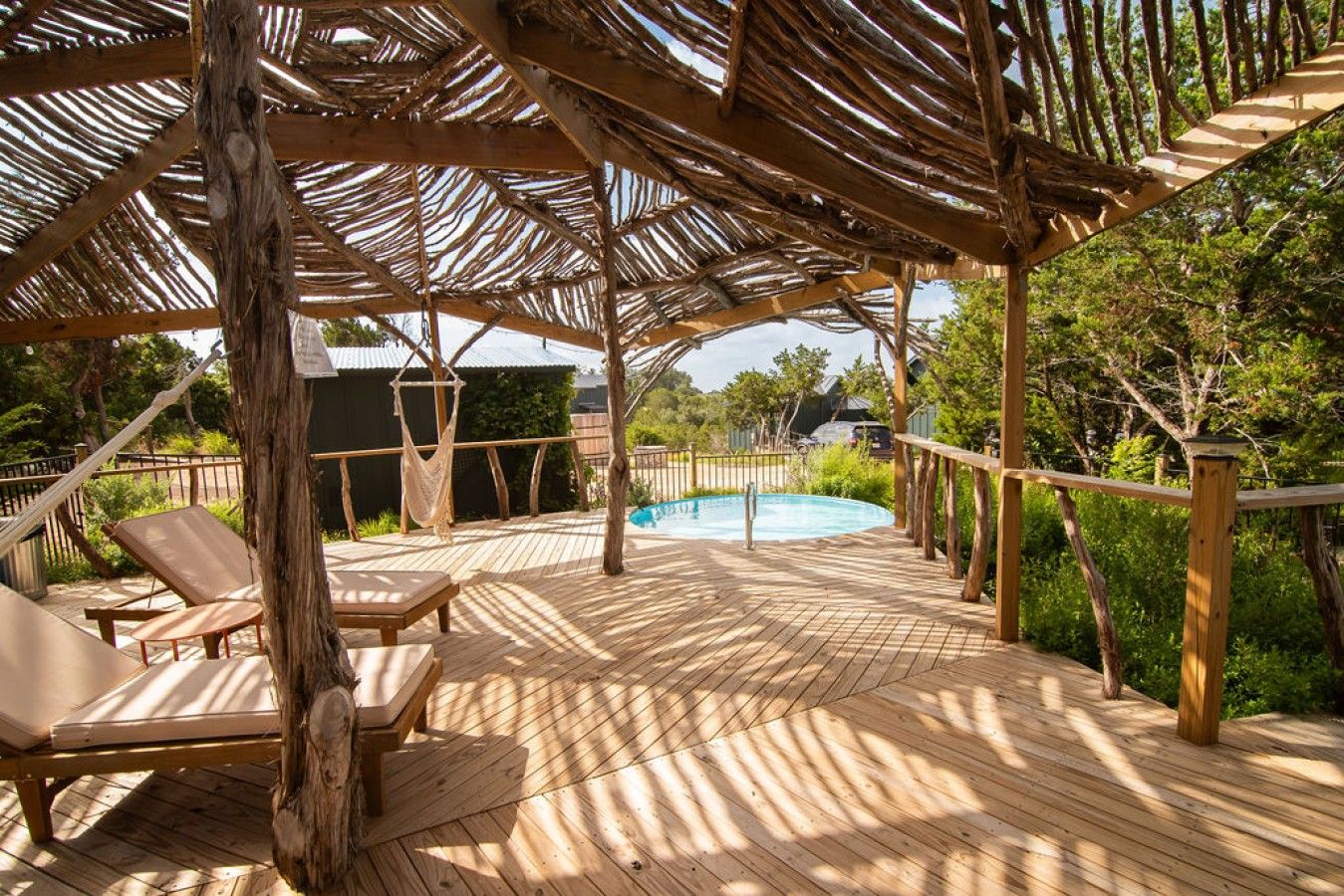 A wooden deck with a pool, lounge chairs, and a pergola structure.