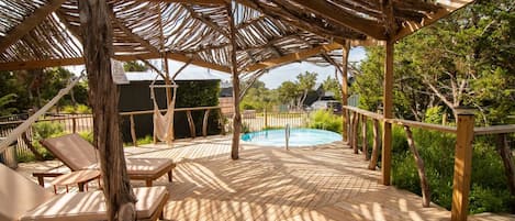 A wooden deck with a pool, lounge chairs, and a pergola structure.