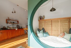 A room with a bed, a wooden cabinet with glassware, and a kitchen area. - Blue Sage No. 12 - The Long Loft Hideaway (Fredericksburg)