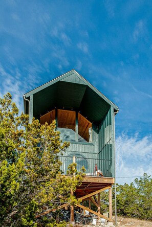 Una cabaña de madera con estructura hexagonal, un balcón y un cielo azul despejado al fondo.