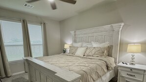 A bedroom with a large bed, two bedside tables, a ceiling fan, and a window with blinds.