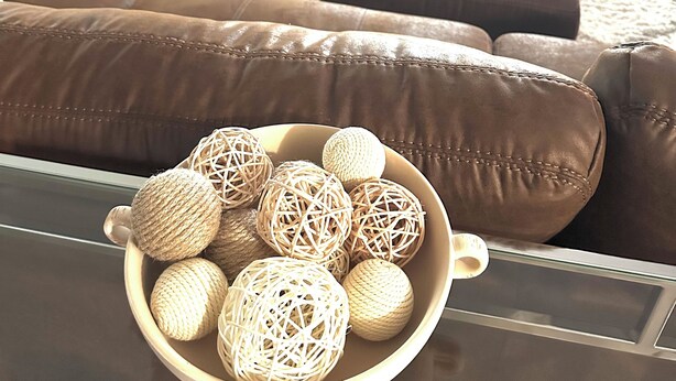 A living room with a brown leather sofa, a glass coffee table, and a bowl of decorative balls.