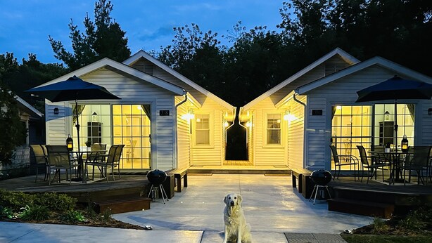 Ein Haus mit überdachter Terrasse, einem Hund und einem Grill.