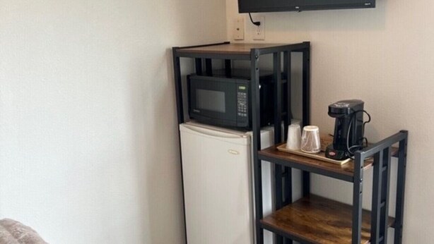 Una habitación compacta con un refrigerador blanco, un microondas, una cafetera y un televisor montado en la pared.