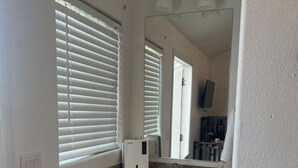 Un baño con lavamanos blanco, armarios de madera, un espejo y una ventana con persianas.