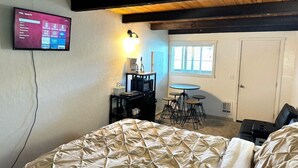A bedroom with a bed, a desk, a chair, a TV, and a window. - Studio Suite #38 River Front (Gold Beach)