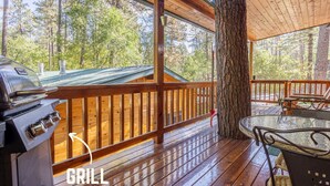 A wooden deck with a grill, a table, and chairs, surrounded by trees. - Homey Cabin with Jacuzzi Near Ski Apache (Ruidoso)