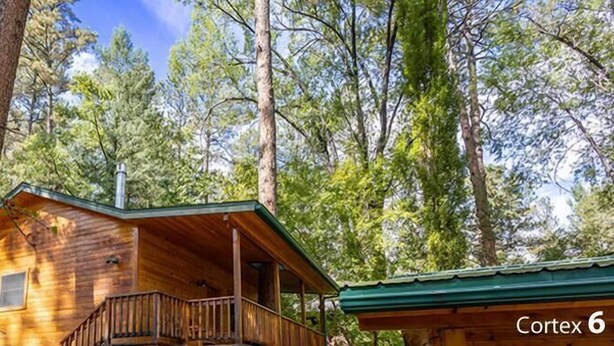 A cabin-style Riverbank Sanctuary with a porch and a viewing deck, surrounded by trees. - Homey Cabin with Jacuzzi Near Ski Apache (Ruidoso)