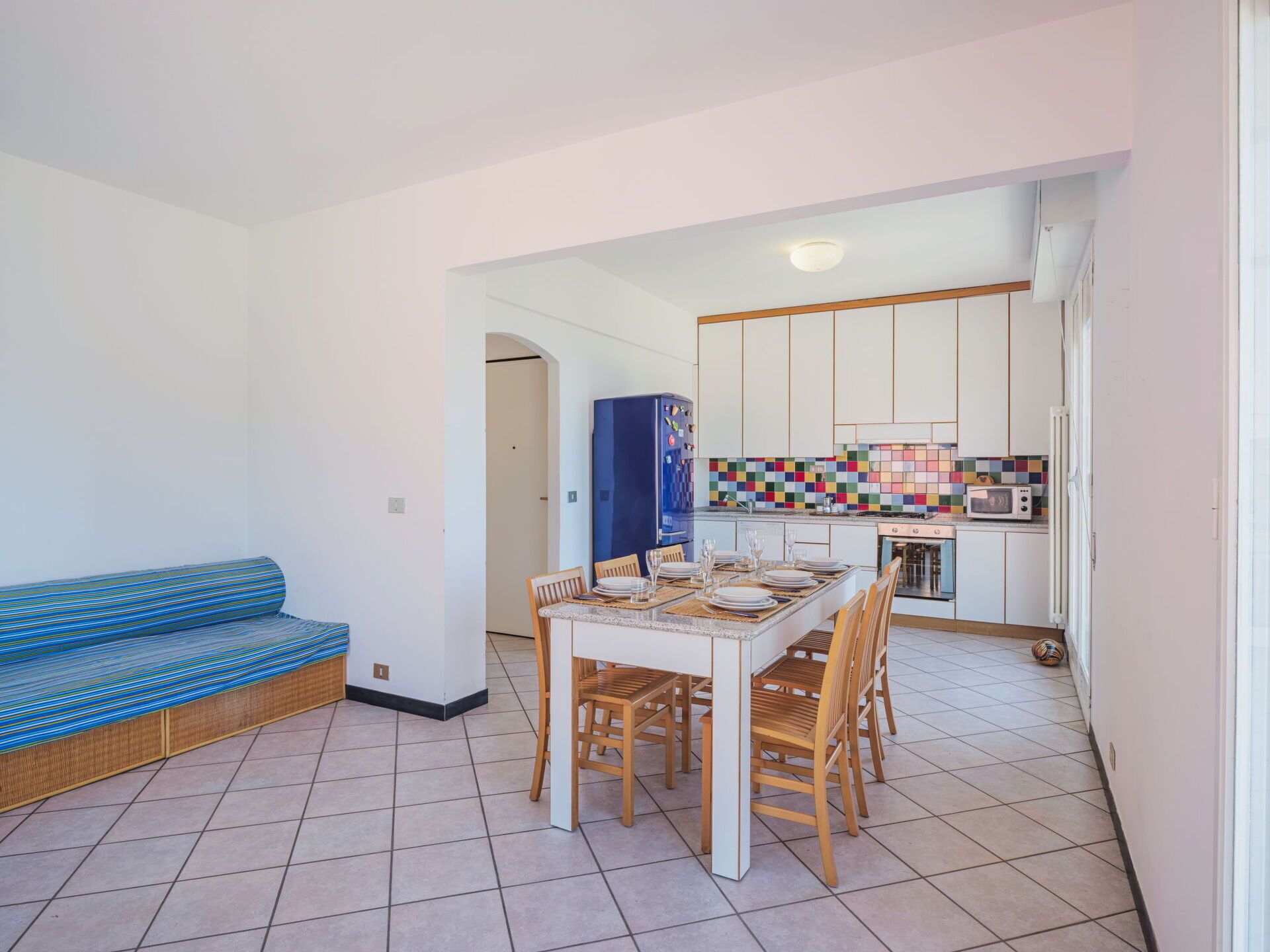 En kompakt opholdsstue med spiseplads, et tekøkken og en lyseblå stribet sofa.