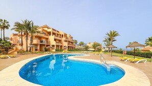 Ein Swimmingpool mit klarem, blauem Wasser, umgeben von Liegestühlen und Palmen.