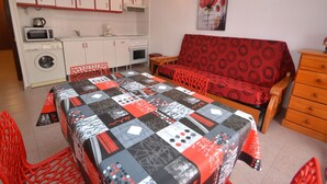 Ein kompakter Wohnbereich mit Küchenzeile, einem Essbereich mit gestepptem Tisch, einer Couch und einem Holzschrank.