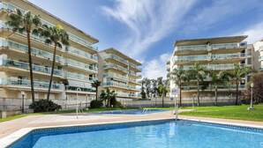 Una piscina con borde de baldosas, rodeada de edificios de varios pisos con balcones y palmeras.