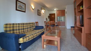 Una sala de estar con un sofá a cuadros, una mesa de centro de vidrio y un televisor sobre un mueble de madera.