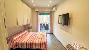 Un dormitorio con cama, televisor y balcón con plantas en macetas.