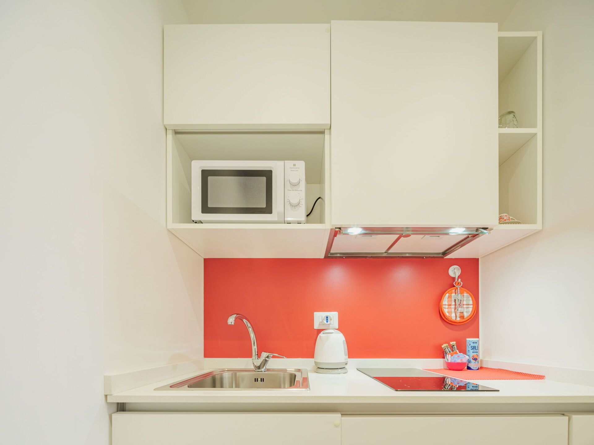 A kitchen with a microwave, a kettle, and a sink.