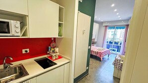 Cocina compacta con microondas, pileta y una pared de acento roja. Se ve un pequeño comedor con mesa y sillas a través de un umbral abierto.