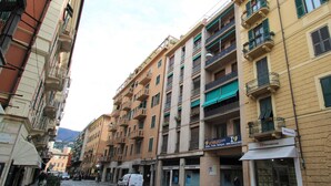 A multi-story building with balconies, a white van parked on the street, and storefronts with signage. - Cosy apartment for 2 guests with A/C, WIFI, TV and balcony (Rapallo)