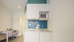 A compact kitchen with white cabinets, a microwave, a sink, and a small table with a colorful tablecloth. - Cosy apartment for 2 guests with A/C, WIFI, TV and balcony (Rapallo)