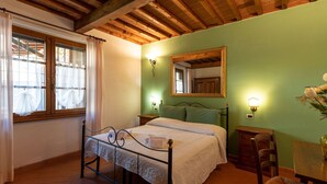 Ein Schlafzimmer mit Bett, Holzboden, grüner Wand, Spiegel und einem Fenster mit Vorhängen.