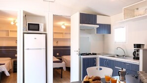 Uma cozinha compacta com micro-ondas, fogão e pia. É visível uma área de refeições com mesa e cadeiras.