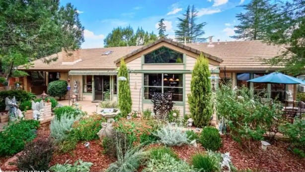 A two-story house with a sloped roof, a front porch, and a garden with various plants and a birdbath.