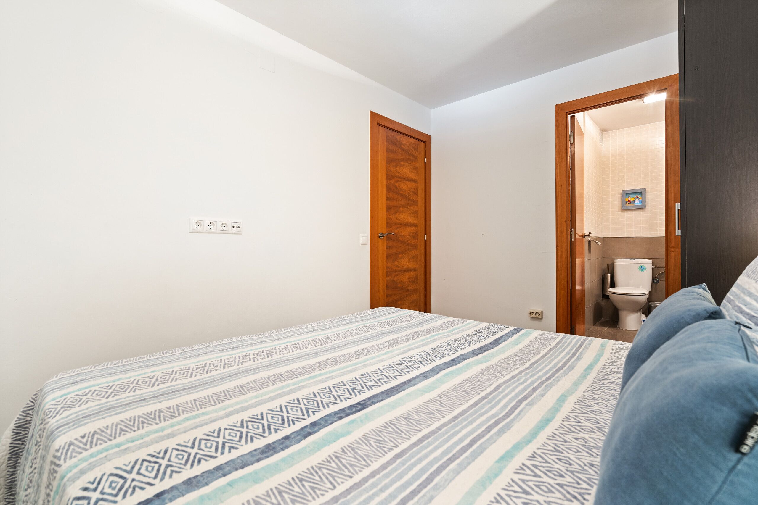 Een slaapkamer met een bed, een houten deur en een zichtbare badkamer door een open deur.