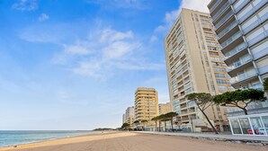 Una playa con edificios altos, cielo despejado y algunos árboles a lo largo del paseo marítimo.