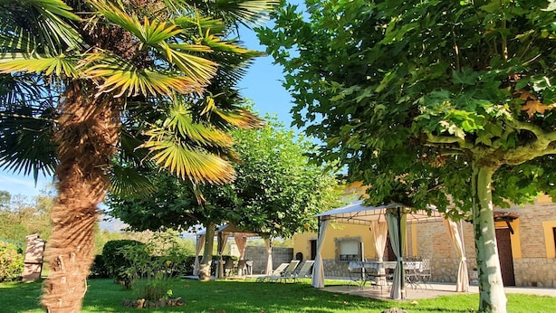 Um jardim com palmeira, um gazebo e um prédio de pedra com mesas ao ar livre.