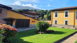 A yellow building with a stone wall, a garage, and a well-maintained lawn. - Casa El Molín 3 Soto de Dueñas (Soto)
