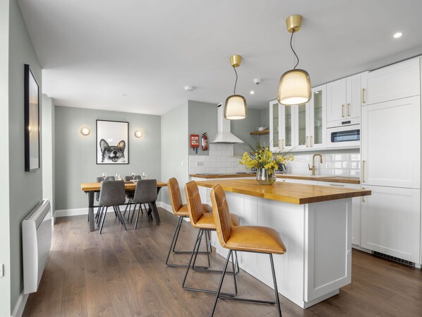 A modern kitchen with a central island, pendant lights, and a dining area with chairs.