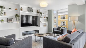 A modern living room with a large flat-screen TV, grey sofas, a coffee table, and a bookshelf with decorative items. - Apartment 295 - Clifden - sleeps 5 guests  in 2 bedrooms (Clifden)