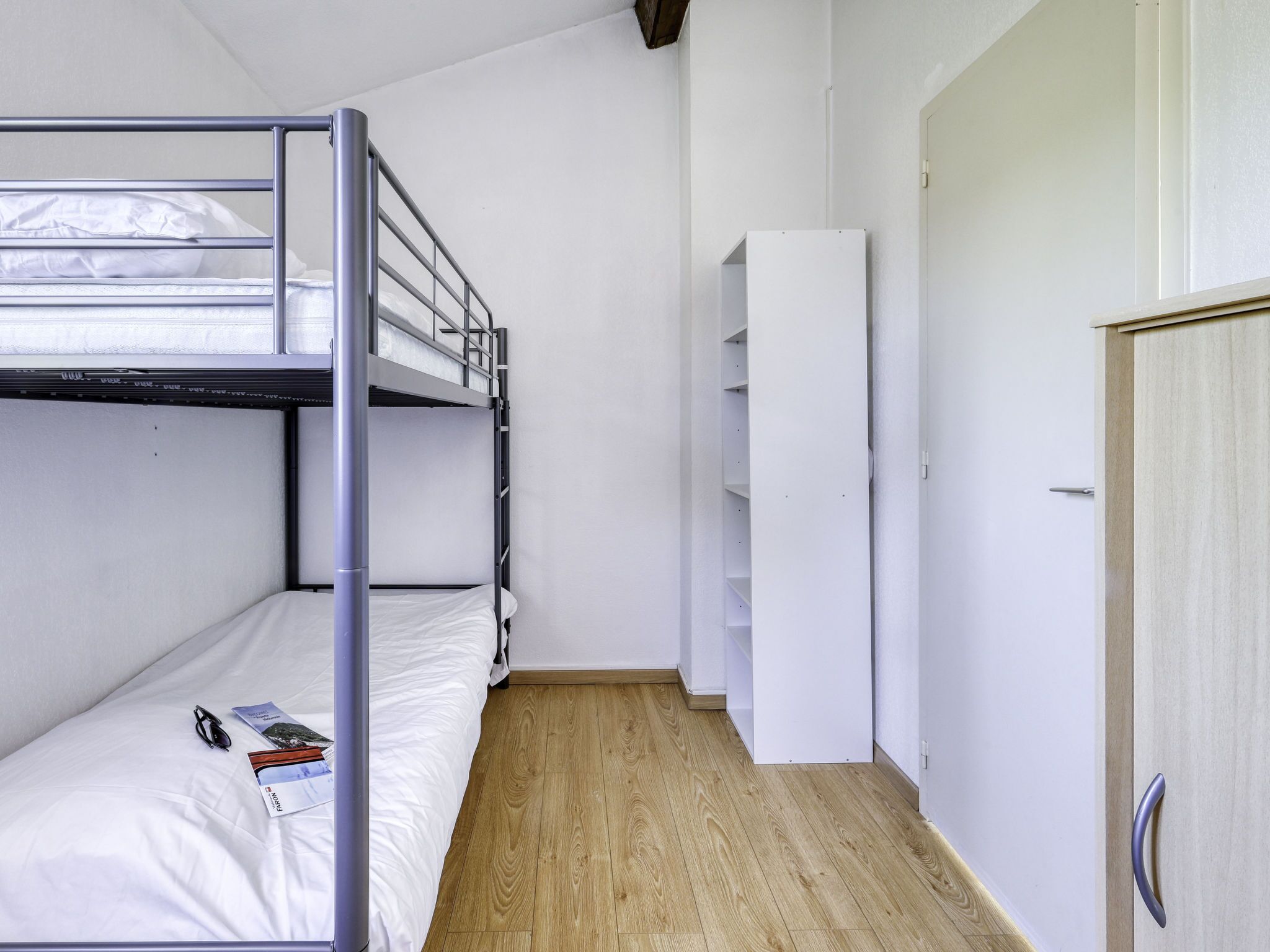 A bunk bed room with a wooden floor, white walls, and a wardrobe.