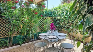 A covered patio with a table and chairs, surrounded by lush greenery and flowering plants. - bonnegrace by Interhome (Six Fours)