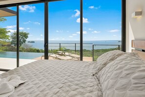Un dormitorio con una cama grande, vista al océano y un balcón con mobiliario exterior.
