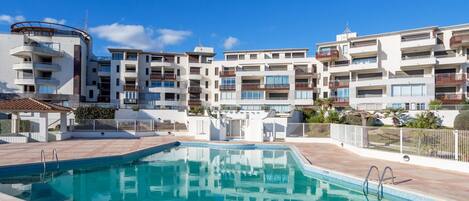 A swimming pool with a tiled deck, surrounded by multi-story residential buildings with balconies and windows.