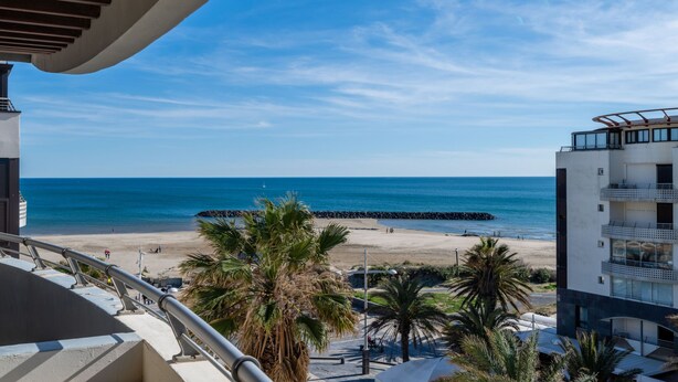 A balcony with a view of a beach, palm trees, and a clear blue sky. - Le Sunset/Cap Sud by Interhome (Cap d'Agde)