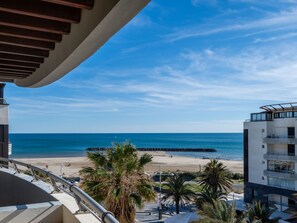 A balcony with a view of a beach, palm trees, and a clear blue sky. - Le Sunset/Cap Sud by Interhome (Cap d'Agde)